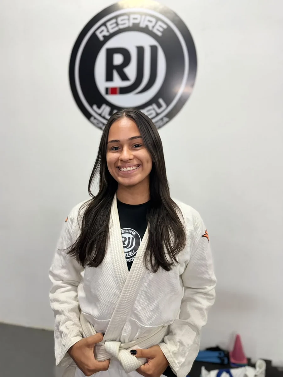 Instrutora Jheniffer com kimono branco em frente à logo da Respire no CT